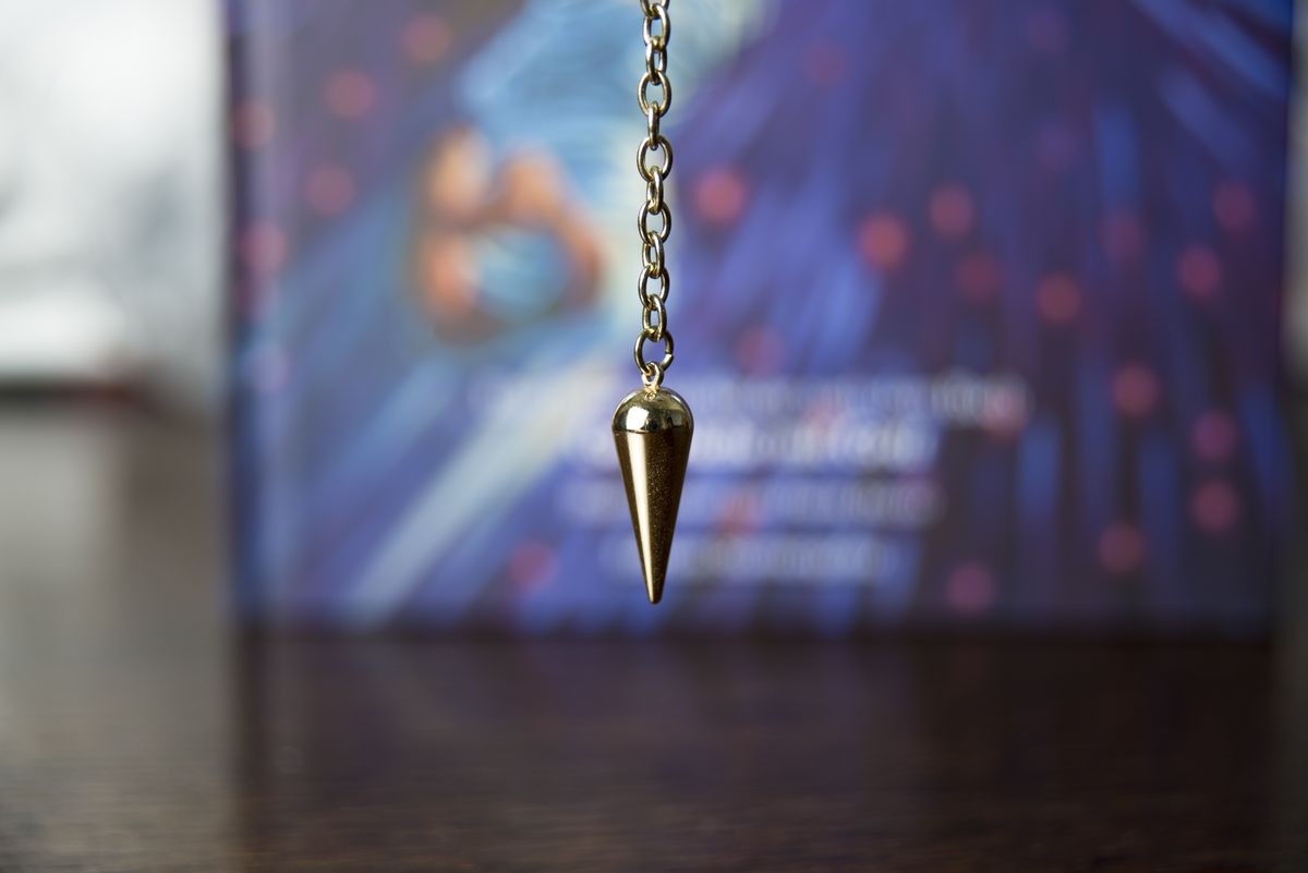 A pendulum photographed in front of an unidentifiable book on a brown table